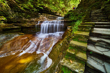 Stone staircase passes by stunning waterfall in Upstate New York with couple in distance