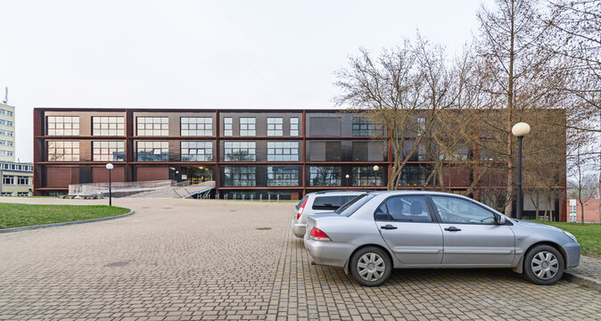 Nowoczesny budynek w mieście. Elewacja wykonana z cortenu. Blacha rdzawa. Duże okna.  Kladka dojściem do wejścia. Polska