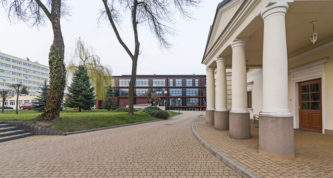 Nowoczesny budynek w mieście. Elewacja wykonana z cortenu. Blacha rdzawa. Duże okna.  Kladka dojściem do wejścia. Polska