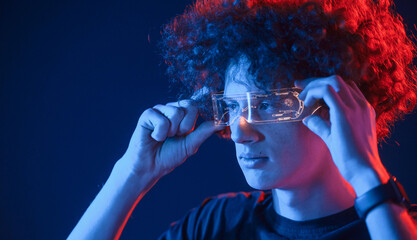 Futuristic eyewear. Young man with curly hair is indoors illuminated by neon lighting