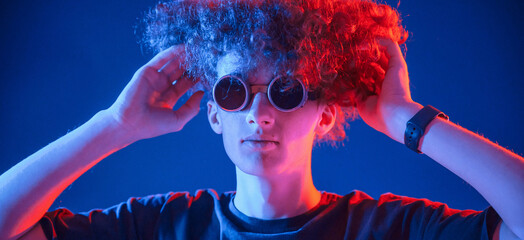 Vintage style glasses. Young man with curly hair is indoors illuminated by neon lighting