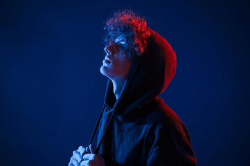 View from the side. Young man with curly hair is indoors illuminated by neon lighting