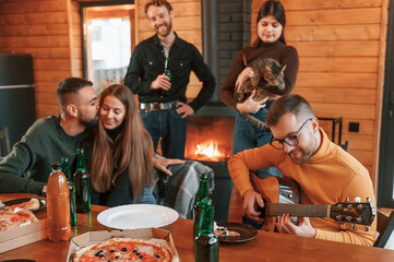Sitting by the table with pizza and beer. Group of friends is having good weekend indoors