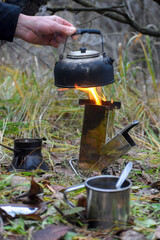 Kettle in a man's hand over a flame from a wood-burning mini stove, outdoor recreation