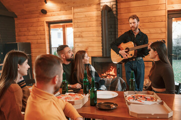 Green bottles with beer and pizza. Group of friends is having good weekend indoors in the wooden building together