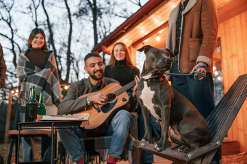 Everyone is looking at the dog. Group of people is spending time together on the backyard at evening time