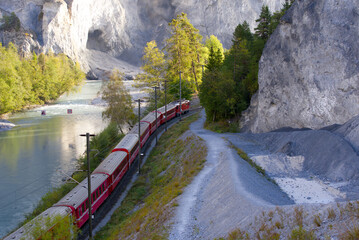 Anterior Rhine valley gorge with Rhine River and red RHB train arriving at railway station...