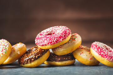 Set of different multicolored sweet donuts donuts with icing and sprinkles on a brown background with copy space
