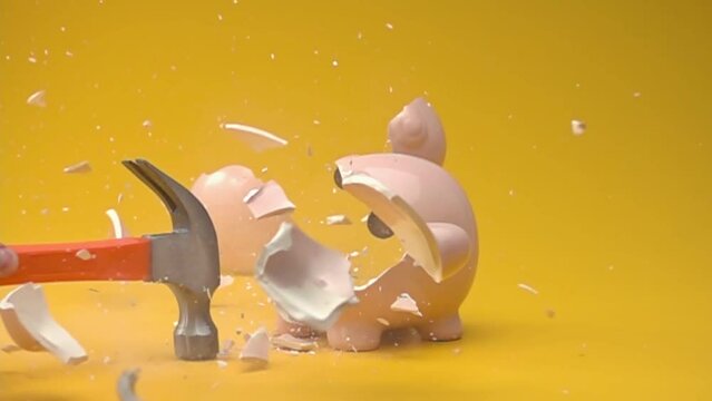 Breaking the piggy bank with hammer. Slow motion.
Piggy bank with money on orange background.