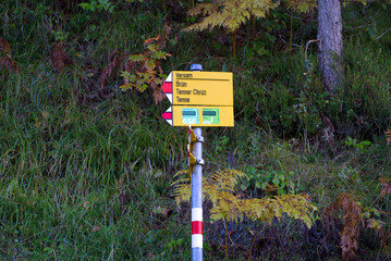 Yellow hiking trail direction signs at mountain village Versam, Canton Graubünden, on a blue cloudy autumn day. Photo taken September 26th, 2022, Versam, Switzerland.