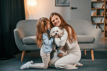 On the floor with pet together. Mother with daughter is at home with maltese dog