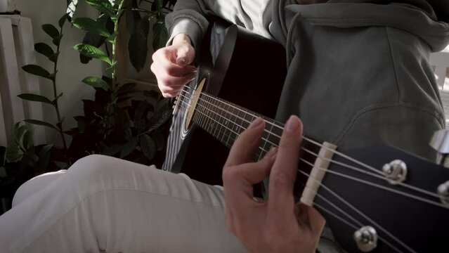 unrecognizable woman singing song and playing acoustic guitar in sunny cottage bedroom, hobby relaxing, girl pinches chords with her fingers