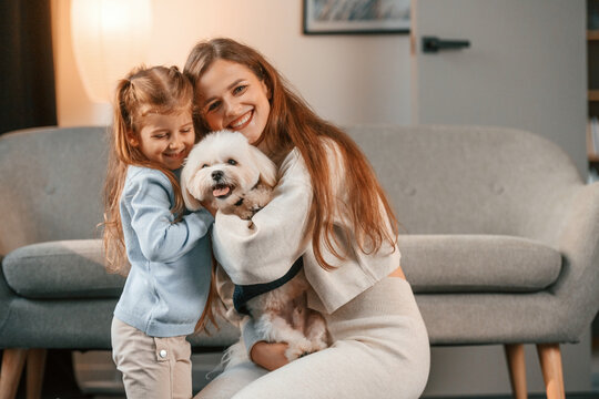 Sitting on the floor. Mother with daughter is at home with maltese dog