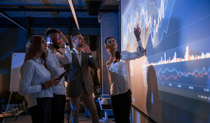 Standing together. Male leader talking to employees, showing the plan on the projector in office of stock exchange company © standret