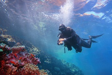Man scuba diver descending from the sea surface to the colorful tropical coral reef.