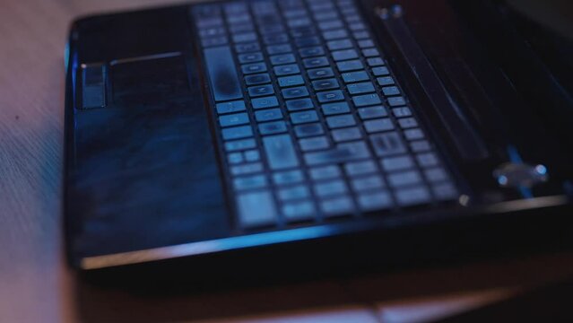 Old-fashioned laptop on a desk in an office. Close-up of hand typing on laptop on desk in dark office, finger touching enter key.