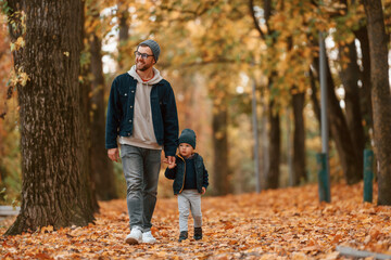 Fototapeta premium Holding each other by the hands. Father and young son is together outdoors at daytime