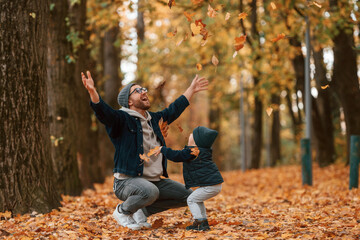 Fototapeta premium Playing with fallen leaves. Father and young son is together outdoors at daytime