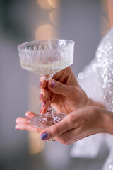 The hands of a woman hold a glass of champagne on a background of golden beke. The concept of the holiday, Christmas, new year, birthday.