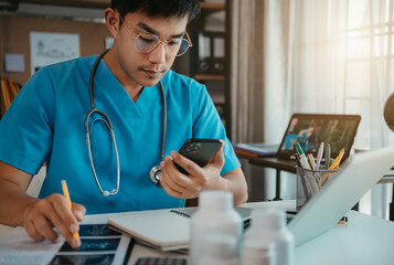 Mid adult male doctor reviews patient records on smartphone and desktop PC.