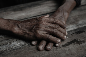 Close-up of old man's hands resting on wood.