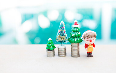 Christmas tree on coin stack with little Santa boy holding gift with space on blurred background, festive season concept