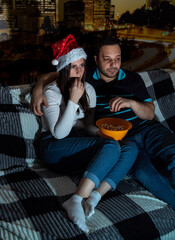 Adult girl and guy are sitting on couch watching TV, eating popcorn. Selective focus. Picture for website about family, leisure.