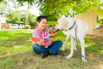 Happy boy giving fruit and eating with his dog friend in the park
