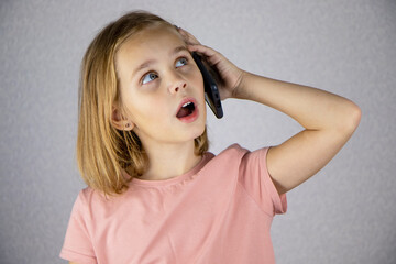 A cute little girl calls on a mobile phone and has an important conversation. Vivid emotions of a child when communicating on a smartphone.