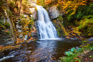 Fototapeta na wymiar Fall foliage surrounds cliffs and huge waterfall over cliffs in peak fall