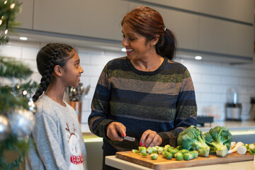 Smiling mother and daughter cutting vegetables in kitchen