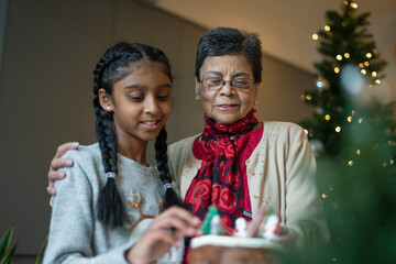 Smiling girl with grandmother decorating Christmas cake - obrazy, fototapety, plakaty