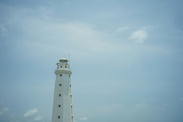 A lighthouse on the beach painted white against a blue sky background