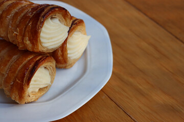 Italian traditional Cannoli filled with vanilla Custard cream on plate on wooden table