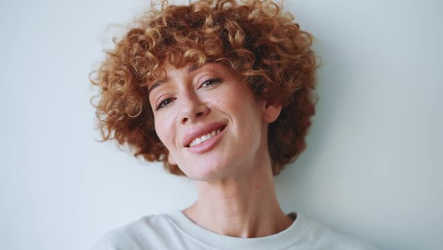 Focused adult curly haired woman looking at the camera in the grey studio