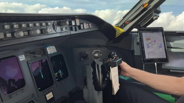 Copilot handling flight controls of a modern jet cockpit overflying some clouds. Side view.