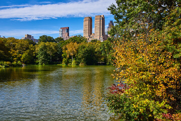 Obraz premium Pond and forests inside Central Park with New York City towering building behind