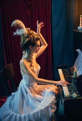 Elegance and tenderness. Portrait of beautiful young woman in image of medieval person in white dress sitting at piano and playing. Comparison of eras, beauty, history, art