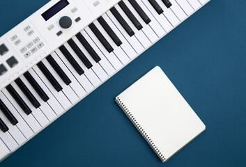 Fototapeta na wymiar Piano keys and blank notepad on blue background, flat lay, copy space.