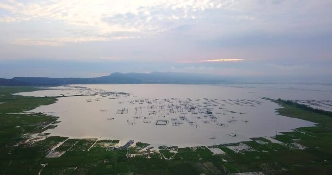 Aerial view of lake with fish cage surrounded by rice fields during sunrise sky - RAWA PENING LAKE, INDONESIA.