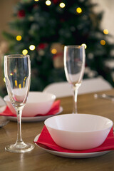 Beautiful table setting for Christmas dinner with transparent glasses, china plates and red napkins against Christmas tree background.
