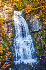 Fototapeta na wymiar Straight on huge waterfall over cliffs with harsh light and fall foliage around