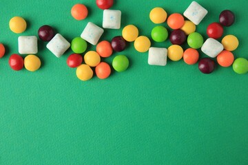 Different tasty chewing gums on green background, flat lay. Space for text