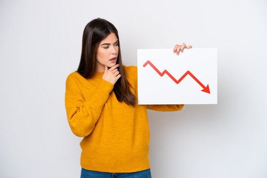 Young Brazilian woman isolated on white background holding a sign with a decreasing statistics arrow symbol and thinking