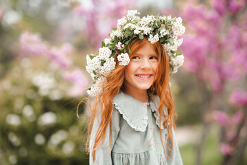 Cute laughing little kid girl 3-4 year old with long curly red hair wear floral wreath and stylish...