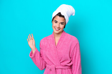 Young Brazilian woman with a bathrobe isolated on blue background saluting with hand with happy expression