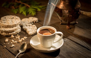 Still life, a cup of hot coffee and a coffee pot standing on a wooden table lit by a ray of morning sun