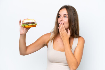 Young pretty woman holding a burger isolated on white background with surprise and shocked facial expression