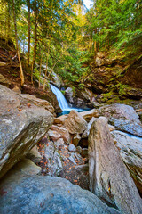 Large boulders near stunning waterfall with blue waters and cliffs covered in fall trees