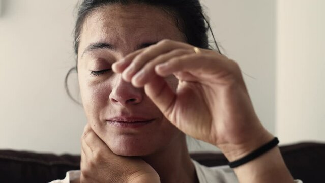 Desperate woman crying suffering from illness. Portrait of a sad anxious female person rubbing face
